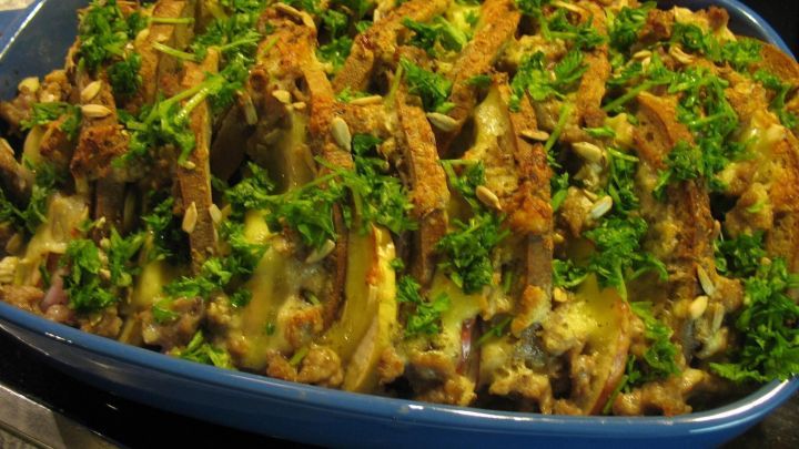 Ein brauner Brotauflauf mit knuspriger Kruste und frischem Gr&uuml;n obendrauf wird in einer blauen Auflaufform pr&auml;sentiert.