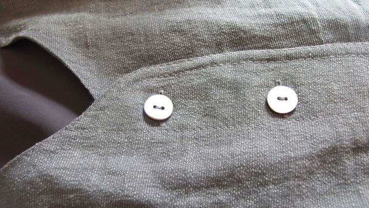 Ein gr&uuml;nes Hemd liegt flach und zeigt zwei wei&szlig;e Kn&ouml;pfe, w&auml;hrend es auf einer Tischoberfl&auml;che drapiert ist.