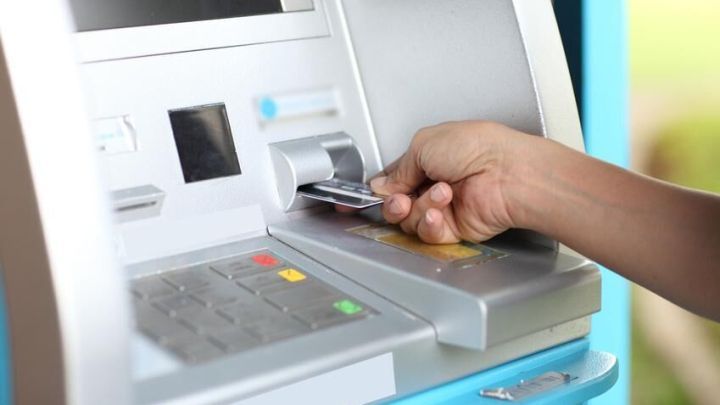 Hand zieht Karte aus Geldautomat im Freien, bereit zur Eingabe von PIN-Nummern am Tastenfeld.