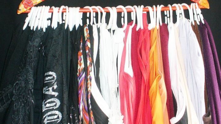 Ein Kleiderb&uuml;gel h&auml;lt viele Tops platzsparend, ordentlich angeordnet, vor einem schwarzen Hintergrund.