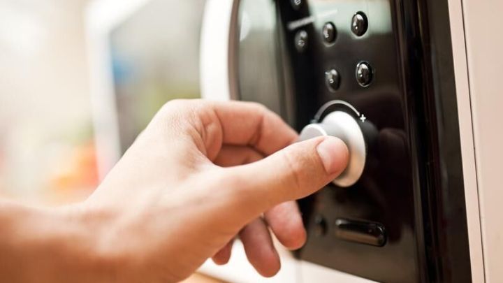 Eine Hand dreht den Knopf einer Mikrowelle, umgeben von einem modernen K&uuml;chenumfeld.