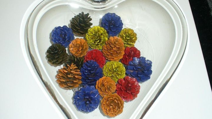 Bunte Zapfen liegen in einem herzf&ouml;rmigen Glasbeh&auml;lter und sorgen f&uuml;r eine moderne Dekoration auf einem wei&szlig;en Tisch.