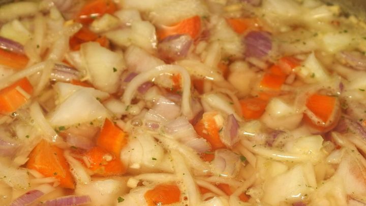 Zwiebeln und Paprika k&ouml;cheln in einem Topf, um beim Kochen Zeit zu sparen, in einer hellen K&uuml;chenszene.