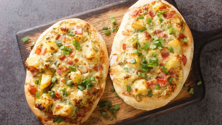 Zwei Winzerwecken mit goldbrauner Kruste, belegt mit Gem&uuml;se und Schinken, liegen auf einem Holzbrett.