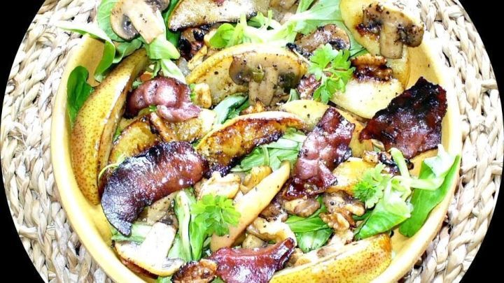 Ein bunten Salat mit frischem Gem&uuml;se und gebratenem Speck, serviert in einer runden Sch&uuml;ssel auf einem geflochtenen Untersetzer.