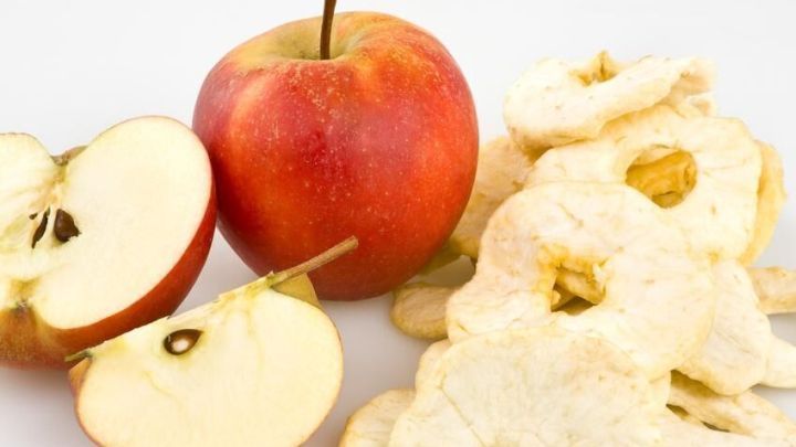 Ein ganzer Apfel steht neben geschnittenen &Auml;pfeln und Apfelringen auf einer hellen Unterlage, bereit zur Apfelchips-Herstellung.