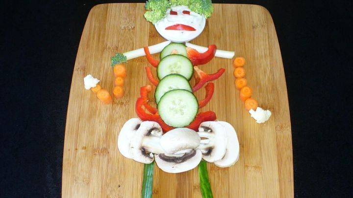 Ein aus Gem&uuml;se gestaltetes Skelett liegt auf einem Holzbrett, umgeben von einer Halloween-Dekoration.