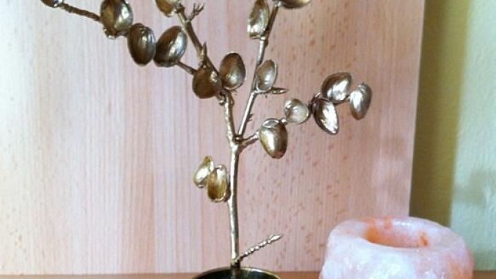 Ein kn&ouml;cherner Dekobaum aus Pistazienschalen steht in einem Topf neben einer rosa Salzkugel auf einem Holztisch.