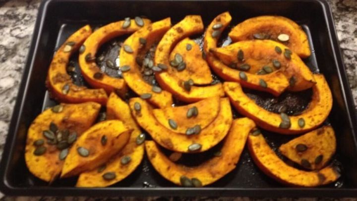 W&uuml;rzige K&uuml;rbisspalten sind auf einem Backblech angerichtet, umgeben von einer rustikalen K&uuml;chenoberfl&auml;che und bereit zum Servieren.