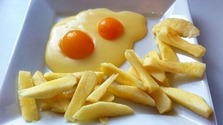 Ein Spiegelei mit zwei Eigelben liegt auf einem Teller, umgeben von Apfel Pommes, die wie frittierte Kartoffeln aussehen.