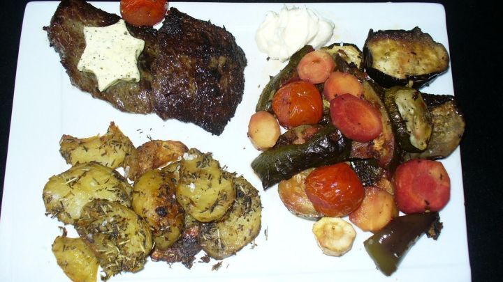 Auf einem wei&szlig;en Teller liegt ein saftiges Rindersteak, umgeben von gebackenem Sp&auml;tsommergem&uuml;se wie Karotten und Zucchini.