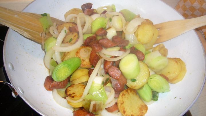 Eine bunte Herbstpfanne mit Kartoffeln, Porree und Mettw&uuml;rstchen dampft in einer Pfanne, bereit zum Servieren.