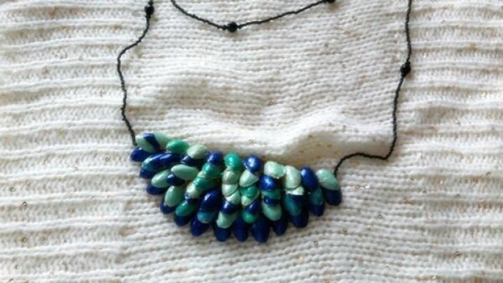 Bunte Pistazienschalen formen eine Halskette, die auf einem hellen, strukturierten Stoff liegt, umgeben von nat&uuml;rlichem Licht.