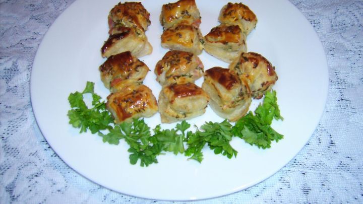 Kleine, gebratene Petersilienschleifen mit Schafsk&auml;se liegen auf einem wei&szlig;en Teller, umgeben von frischem Gr&uuml;n.