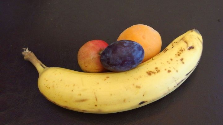 Ein Obstsalat mit einer Banane, Pflaume und Aprikose liegt auf einer dunklen Oberfl&auml;che und zeigt herbstliche Farben.