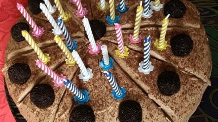 Eine Schokosahne Torte mit vielen bunten Kerzen steht auf einem dekorativen Teller, umgeben von rotem Tischdeckenmaterial.