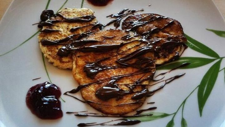 Bananenpfannkuchen liegen mit Schokoladensauce verziert auf einem Teller, umgeben von Klecksen roter Marmelade.