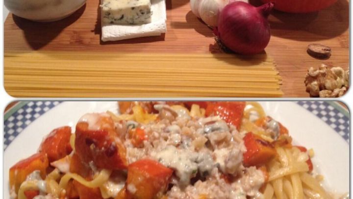 Pasta liegt auf einem Teller, bedeckt mit K&uuml;rbisst&uuml;cken in einer Gorgonzola-Walnuss-Sauce, umgeben von frischen Zutaten.