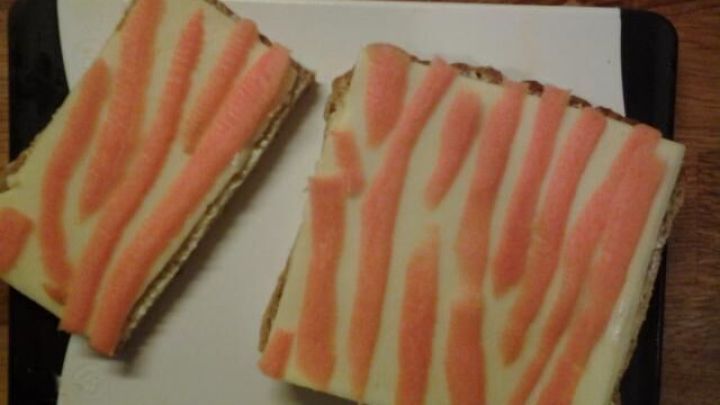 Zwei farbenfrohe Tigerstullen mit K&auml;se und M&ouml;hren-Dekor liegen auf einem Schneidebrett in einer gem&uuml;tlichen K&uuml;chenszene.