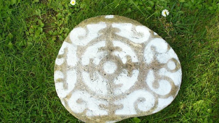 Eine verzierte Beton Gehwegplatte liegt auf gr&uuml;nem Gras, geschm&uuml;ckt mit einem eleganten Muster in Wei&szlig;.