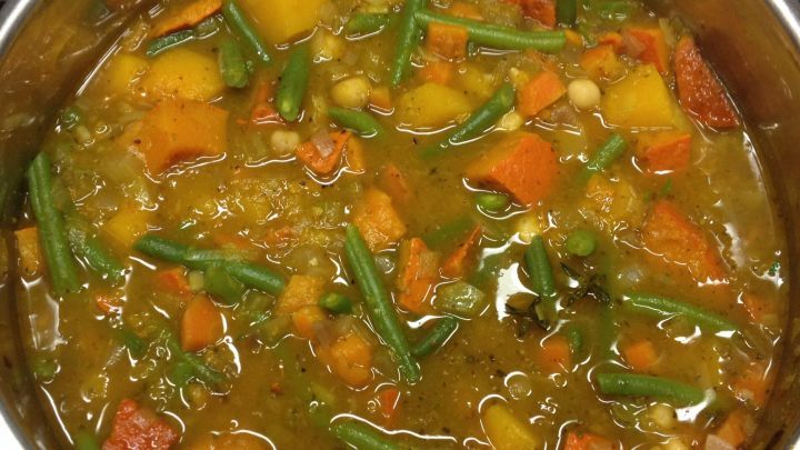 Ein bunter K&uuml;rbiseintopf kocht in einem Topf, gef&uuml;llt mit K&uuml;rbisst&uuml;cken, Gem&uuml;se und gr&uuml;nen Bohnen, auf der Herdplatte.