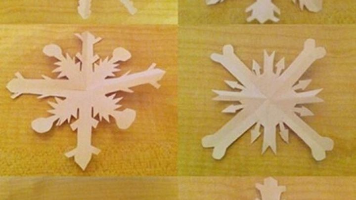 Sechs kunstvoll gefaltete Schneeflocken aus Papier liegen auf einem hellen Tisch, bereit zum Basteln und Dekorieren.