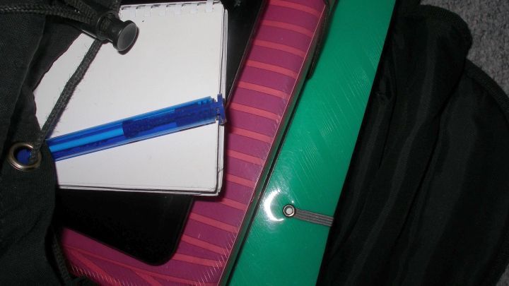 Ein gr&uuml;ner Aktentasche liegt offen und enth&auml;lt einen Notizblock und einen blauen Stift, bereit f&uuml;r das Falten von Hemden oder Blusen.