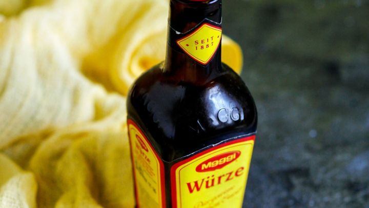 Eine Flasche Maggi-W&uuml;rze steht auf einer dunklen Oberfl&auml;che, umgeben von einem gelben Tuch, das einen gem&uuml;tlichen Kontext schafft.