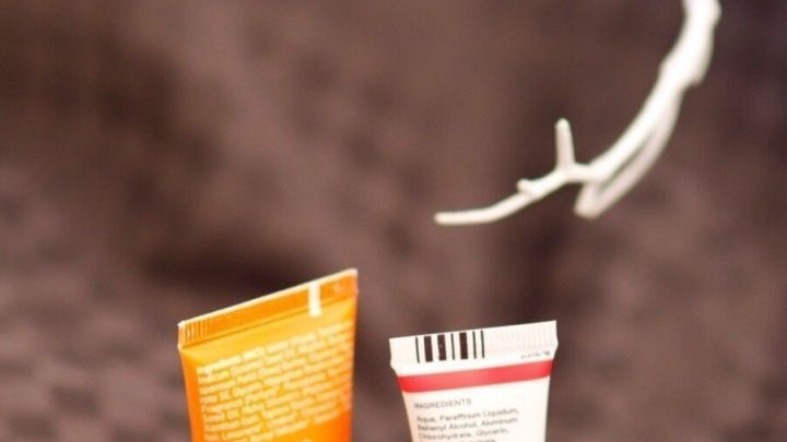 Drei Gesichtspflegeproben stehen auf einem checkered-taupefarbenen Hintergrund, umgeben von einer wei&szlig;en &Auml;ste-Dekoration.