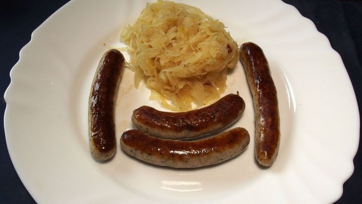 Bratw&uuml;rste liegen gebraten auf einem wei&szlig;en Teller neben einer Portion Sauerkraut, arrangiert in herzhaftem Ambiente.