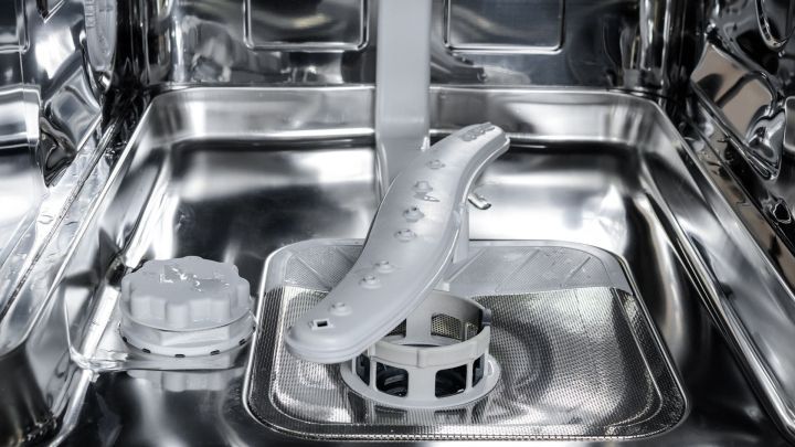 Eine Sp&uuml;lmaschine mit einem sauberen Spr&uuml;hstab und Abflussgitter im gl&auml;nzenden Innenraum, bereit f&uuml;r die Reinigung.
