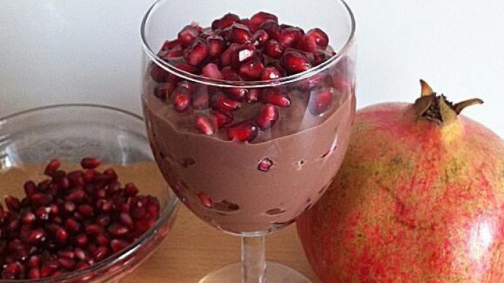 Eine elegante Schale enth&auml;lt Nougatmousse, garniert mit frischen Granatapfelkernen, neben einer ganzen Granate.