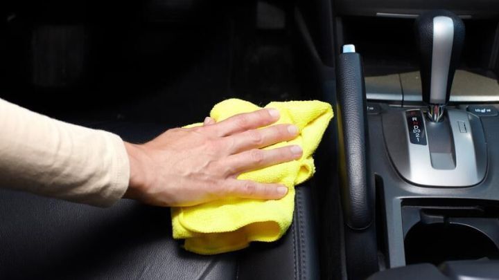 Hand wischt mit gelbem Tuch den Autositz in einem Fahrzeug, um Schmiere zu entfernen, nahe der Gangschaltung.