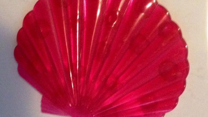 Eine rot-transparente Anti-Rutsch-Figur in Muschelform liegt auf einer wei&szlig;en Oberfl&auml;che und wartet auf die Reinigung.