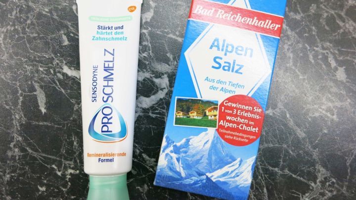 Zwei Produkte stehen auf einer dunklen, marmorierten Oberfl&auml;che: Zahnpasta und Salz, bereit zum Reinigen von K&uuml;chenschr&auml;nken.