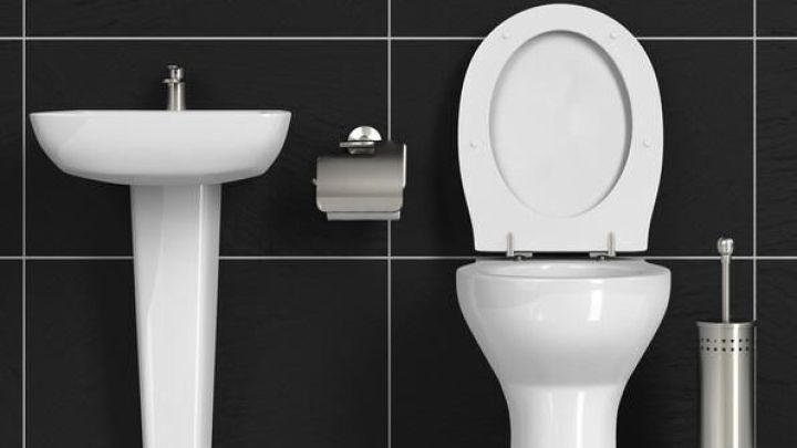 Toilette steht offen neben Waschbecken und Papierspender in einem Bad mit schwarzen Fliesenw&auml;nden.