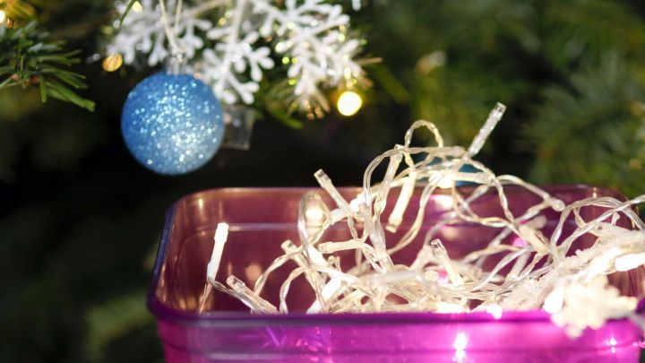 Ein k&uuml;nstlerisch dekorierter Beh&auml;lter bewahrt Lichterketten auf, w&auml;hrend ein Weihnachtsbaum im Hintergrund schimmert.