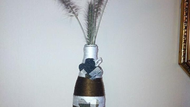 Eine dekorative Flasche steht auf einem Tisch und zeigt geschmackvoll arrangierte Gr&auml;ser als Blumenvase.