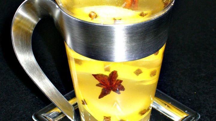 Ein Glas orientalischer Tee mit Zimtstange, Sternanis und Nelken steht auf einem silbernen Untersetzer auf schwarzem Tisch.