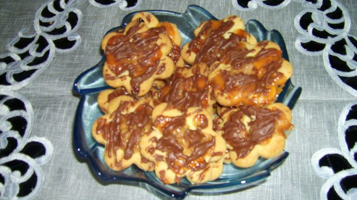 Auf einem blauen Teller liegen frisch gebackene Karamellpl&auml;tzchen mit Nugatstreifen, umgeben von einem wei&szlig;en Tischtuch.