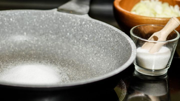 Eine Pfanne liegt auf einer Herdplatte, daneben steht eine Schale mit Zwiebeln und ein Glas mit Salz, bereit zum Kochen.