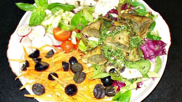 Ein bunten Salatteller mit frischem Gem&uuml;se, Maultaschen und H&auml;hnchenbrustfilet auf einem wei&szlig;en Teller, ansprechend angerichtet.