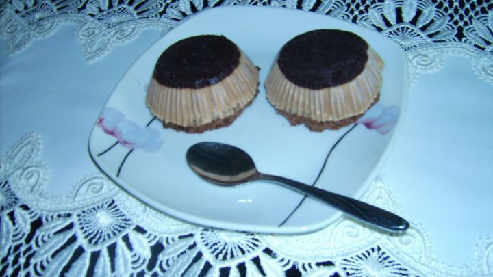 Zwei Schwarzbiersahne T&ouml;rtchen stehen auf einem Teller, umgeben von einem dekorativen Tischl&auml;ufer, mit einem L&ouml;ffel daneben.