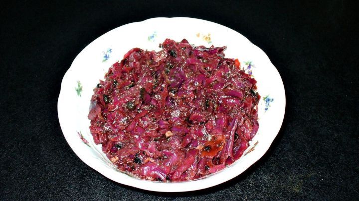 Gew&uuml;rzrotkohl in einer Sch&uuml;ssel, gl&auml;nzend und rot-violett, bereit f&uuml;r eine festliche Mahlzeit, umgeben von einer dunklen Tischoberfl&auml;che.