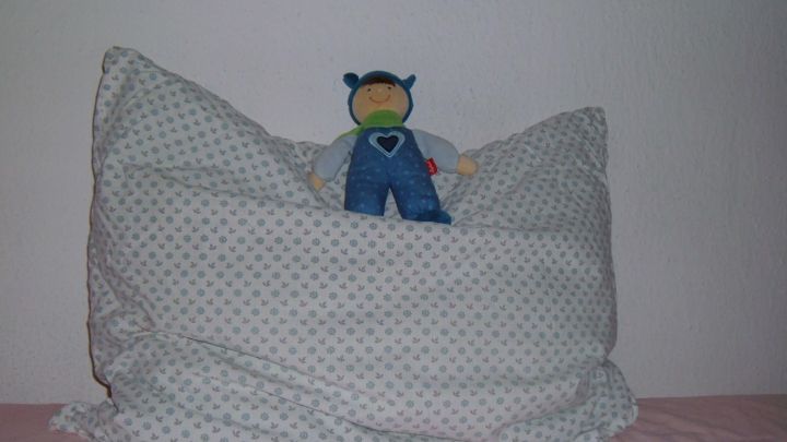 Ein Federbett mit einem bunten Kissenbezug liegt auf einem Bett, w&auml;hrend ein Spielzeug darauf sitzt.