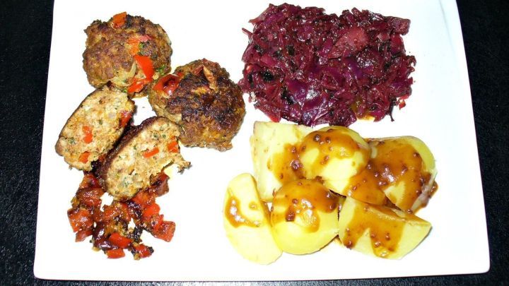 Leckere Frikadellen mit Gem&uuml;se liegen auf einem wei&szlig;en Teller, umgeben von Rotkohl und mit glasierten Kartoffeln.