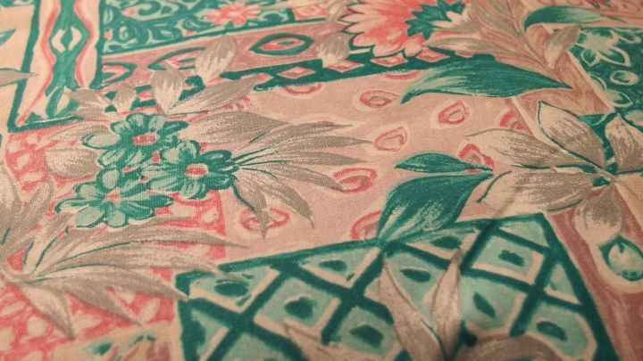 Ein bunter Stoff mit floralem Muster liegt flach auf einer Oberfl&auml;che und zeigt verschiedene gr&uuml;ne und rosafarbene Designs.