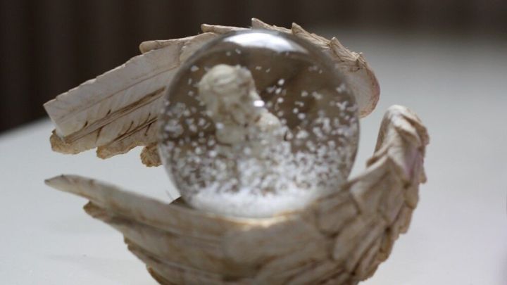 Eine Schnee-globe mit einer Engelstatue in einer gefl&uuml;gelten Hand, umgeben von einer hellen, ruhigen Umgebung.