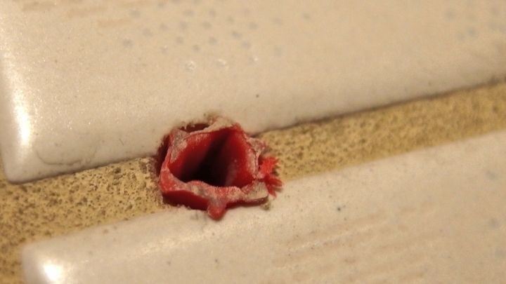 Ein D&uuml;bel ist teilweise aus einer Wand auf einer Oberfl&auml;che herausgezogen, umgeben von Fliesen.