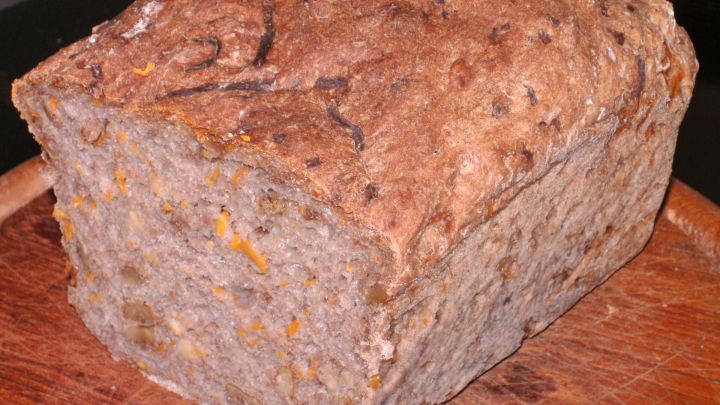 Ein rustikales Brot mit Hokkaidok&uuml;rbis und Waln&uuml;ssen liegt auf einem Holzteller, bereit zum Servieren oder Essen.